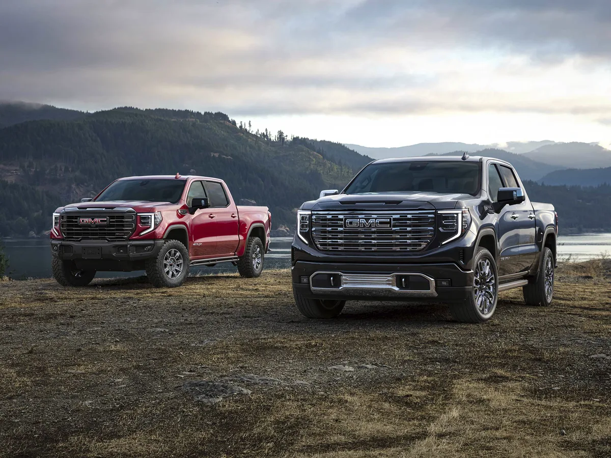Front View of Two 2026 GMC Sierra 1500 Pickup Trucks Parked in a Grassy Field by a Body of Water