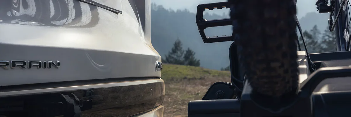 A Close-Up View of the Rear Bumper of a White GMC SUV with a Bike Rack Holding a Bicycle Wheel