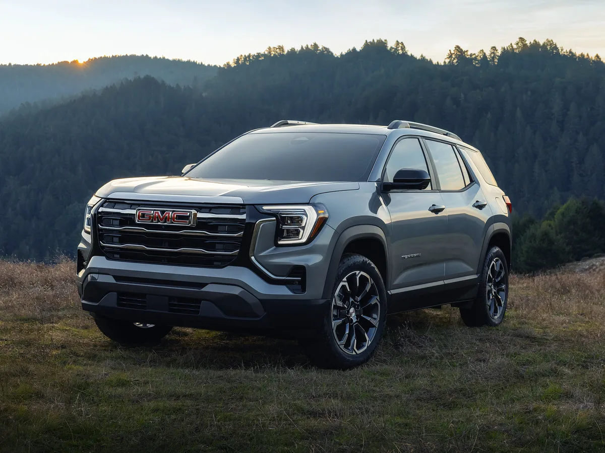 A Gray GMC Denali SUV Parked in a Grassy Field with Forested Hills and a Sunset in the Background